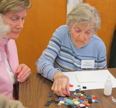Penny Marinakis receives assistance with creating her mosaic by Mosaic Society volunteer, Carol Hemsley.