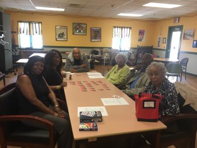 Bill Jones, Anna Garvins, Walter Brown, and Gloria Thompson participate in a memory card game with presenters, Paula and Carole on the left. 