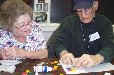 Schoolhouse Mosaic class student and program volunteer, Kathy Thompson, assists Tom Ennis with his mosaic. 